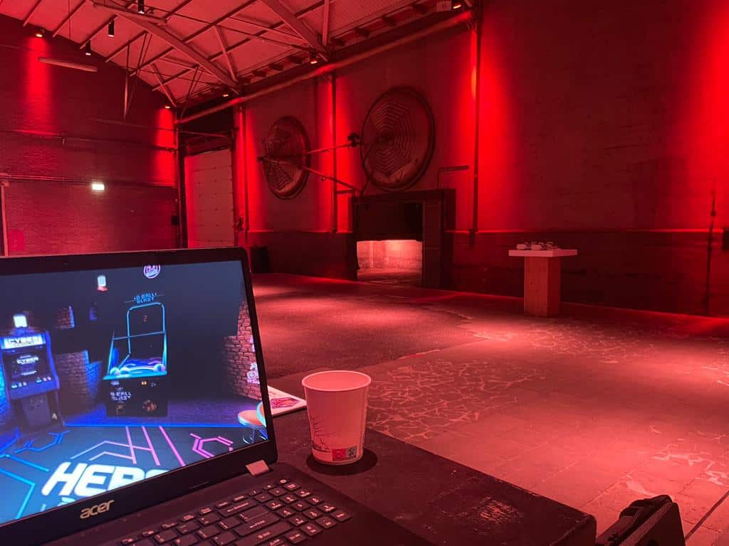 Laptop showing a VR arcade game on screen in a red-lit event venue.
